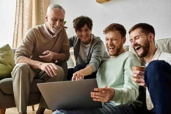 A gay couple and parents share a laugh while looking at a laptop. — Stock Photo