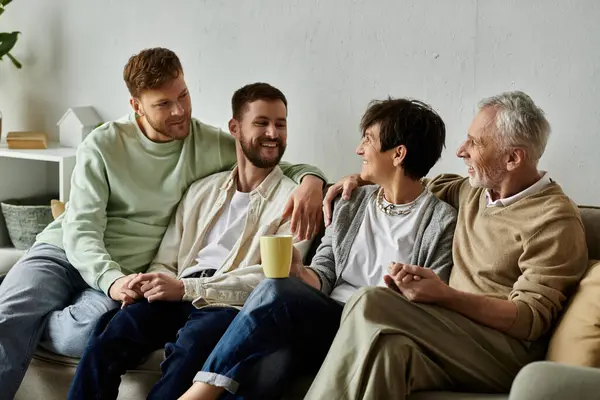 A gay couple sits on a couch with parents in a home setting, enjoying a conversation and a drink. — Stock Photo