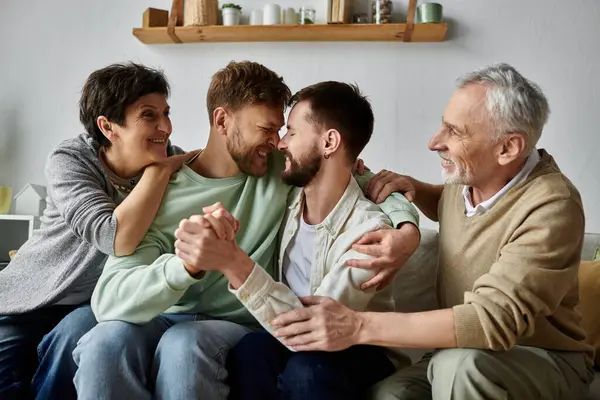 A gay couple sits on a couch with parents, all smiling and embracing each other. — Stock Photo