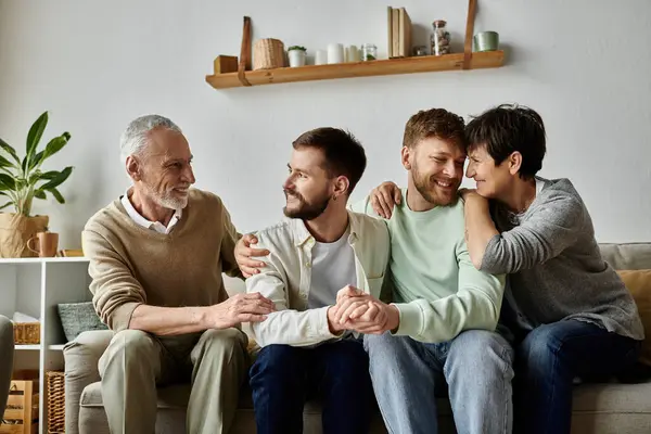 Una pareja gay se sienta con sus padres en un sofá en su casa. - foto de stock