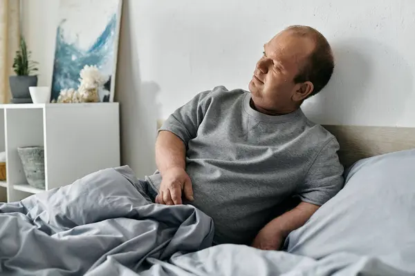 A man with inclusivity sits thoughtfully on a bed, his gaze directed upwards, lost in contemplation. — Stock Photo