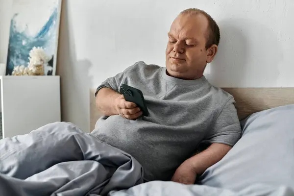 A man with inclusivity sits in bed, using his smartphone, starting his day. — Stock Photo