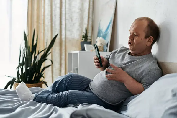 A man with inclusivity in his pajamas is sitting up in bed, using his phone. — Stock Photo