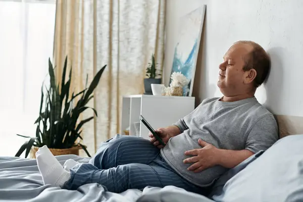 A man with inclusivity reclines on his bed, holding a phone in his hand, seemingly taking a break from his day. — Stock Photo