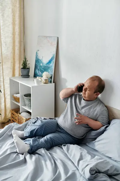 A man with inclusivity sits on a bed, talking on his phone. — Stock Photo