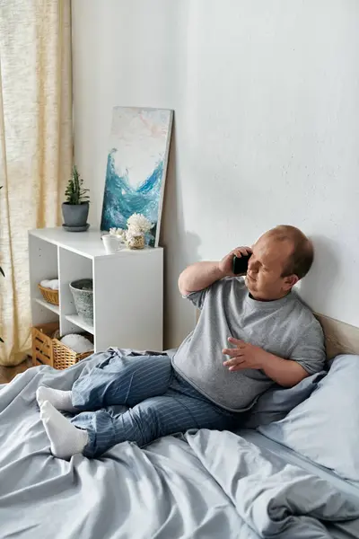 Un hombre con inclusividad se sienta en una cama, hablando por teléfono. — Stock Photo