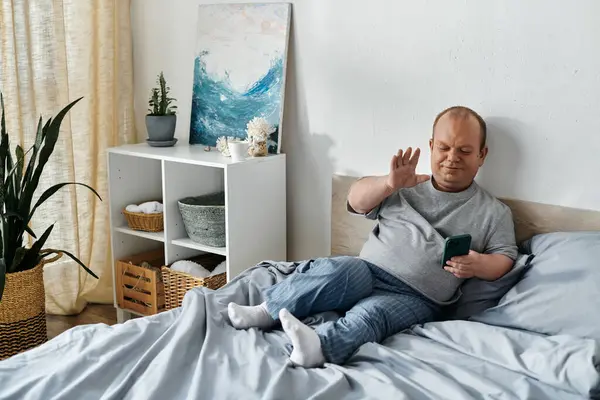 Чоловік з інклюзивністю сидить на ліжку, махаючи по телефону. — стокове фото