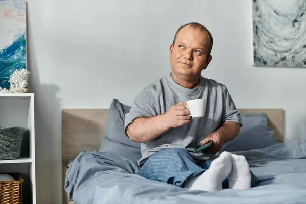 A man with inclusivity sits in bed, enjoying a cup of coffee and his morning routine. — Stock Photo