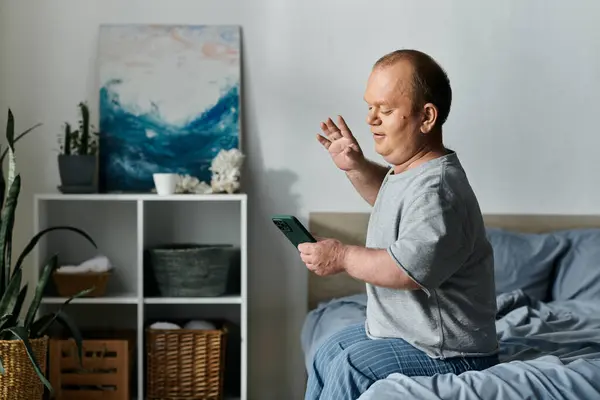 Человек с инклюзивностью сидит на кровати, используя свой телефон, чтобы сделать видеозвонок. — стоковое фото