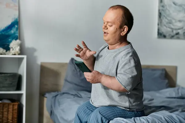 Un homme avec inclusivité s'assoit sur un lit, engagé dans un appel vidéo sur son téléphone, montrant le pouvoir de connexion et d'inclusivité. — Photo de stock