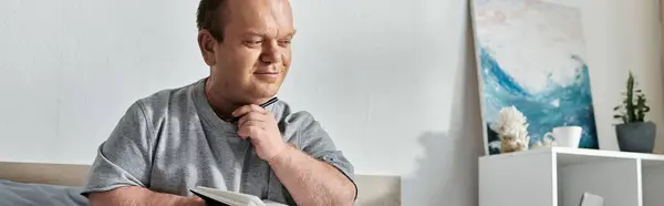 A man with inclusivity sits on a bed, pen in hand, thoughtfully looking down. — Stock Photo