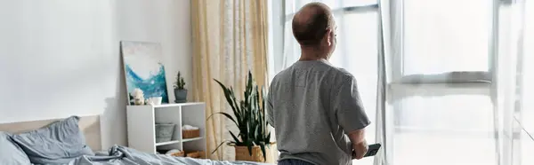 A man with inclusivity stands by a window in a bedroom, looking out at the view. — Stock Photo