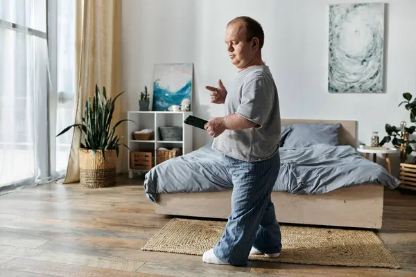 A man with inclusivity stands in his bedroom, holding a phone and smiling. — Stock Photo