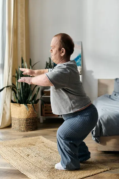 A man with inclusivity performs a squat exercise on a mat in a room with a bedroom in the background. — Stock Photo