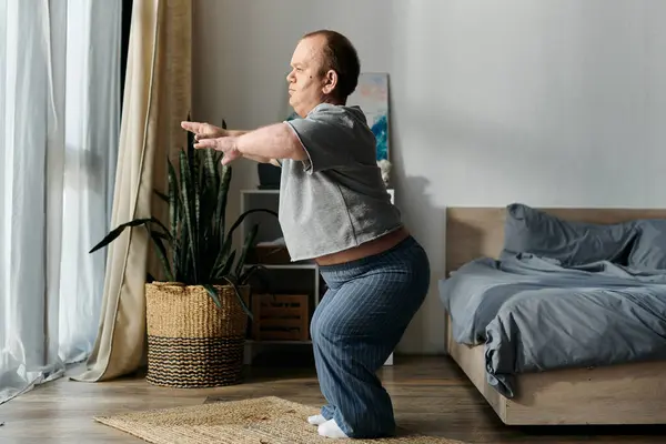 Un hombre con inclusividad se estira en su casa, con una cama y una planta en el fondo. — Stock Photo