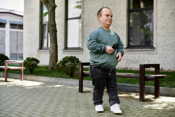 Мужчина с включённостью с телефоном в руке проходит мимо скамейки в городской обстановке. — стоковое фото
