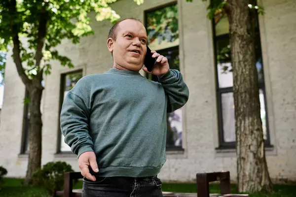 A man with inclusivity in a green sweater talks on his phone outside a building. — Stock Photo