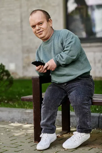 Um homem com inclusividade senta-se em um banco, olhando para o telefone, desfrutando de um momento de paz. — Fotografia de Stock