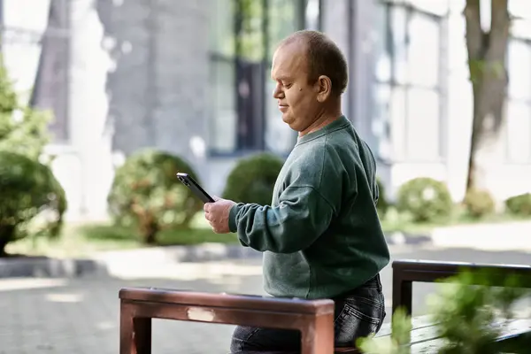 A man with inclusivity is standing near a bench, looking at his phone. — Stock Photo