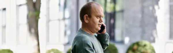 Um homem com inclusividade fica do lado de fora da cidade, falando em seu telefone, enquanto o sol brilha. — Fotografia de Stock