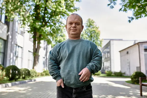 Человек с инклюзивностью стоит на городской улице, улыбается и смотрит в камеру. — стоковое фото