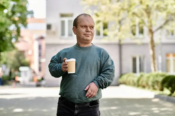 Um homem com inclusividade caminha pela rua, segurando uma xícara de café. — Fotografia de Stock