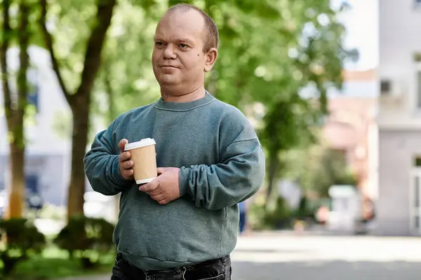 Um homem com inclusão desfrutando de um café em um dia ensolarado em um parque da cidade. — Fotografia de Stock