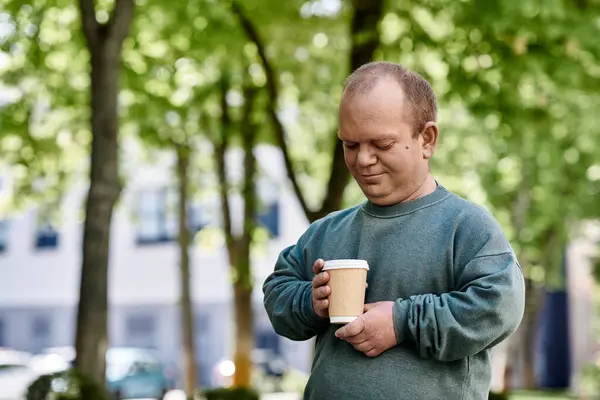 A man with inclusivity stands in a park holding a cup of coffee. — Stock Photo
