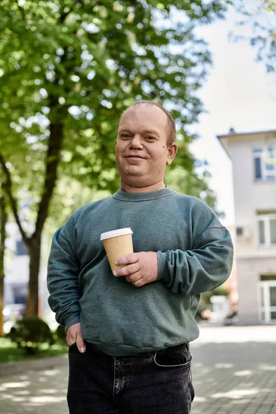 A man with inclusivity with a coffee cup walks in the city park, looking confident and content. — Stock Photo