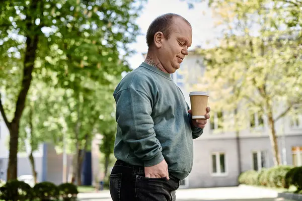A man with inclusivity, holding a coffee cup, walks on a city street. — Stock Photo