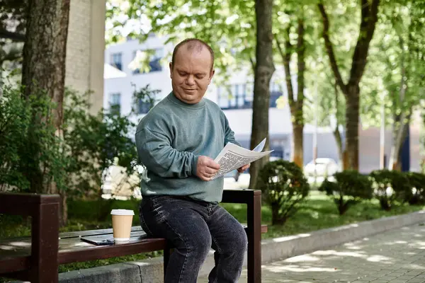 A man with inclusivity sits on a park bench, reading a document and enjoying a cup of coffee. — Stock Photo