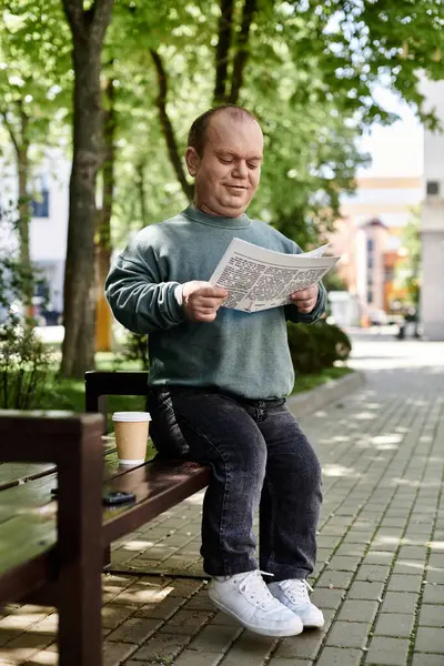 A man with inclusivity sits on a park bench reading a newspaper and enjoying a cup of coffee. — Stock Photo