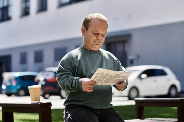 A man with inclusivity sits on a bench outside, reading a newspaper, enjoying a sunny afternoon. — Stock Photo
