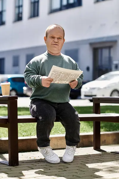 A man with inclusivity sits on a bench in the city, reading a newspaper on a sunny day. — Stock Photo