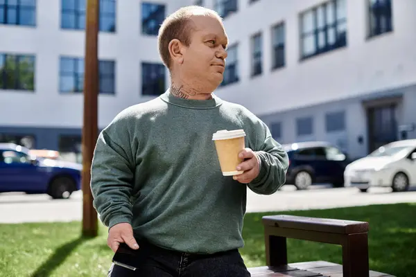 A man with inclusivity walks with a coffee cup in hand, enjoying the urban scenery around him. — Stock Photo