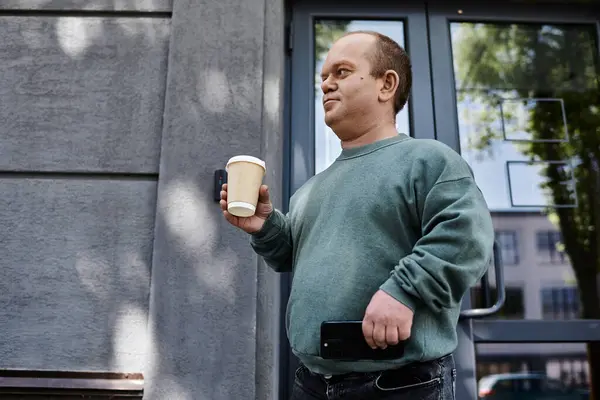 Un homme avec inclusivité dans un pull vert tient une tasse de café en regardant vers sa gauche. — Photo de stock