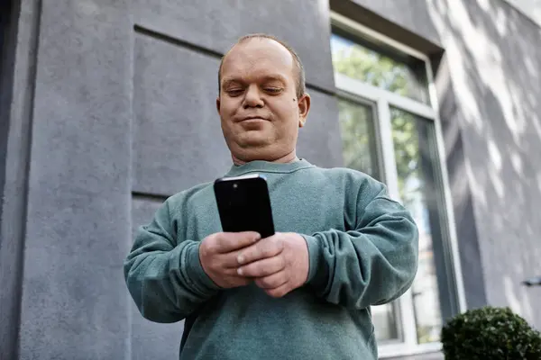 A man with inclusivity in a teal sweater checks his phone while standing on a city street. — Stock Photo