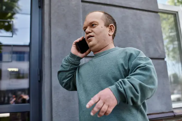 A man with inclusivity in a green sweater uses his phone outside a building. — Stock Photo