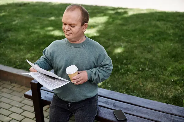 Un homme inclusif s'assoit sur un banc de parc, dégustant une tasse de café et lisant un journal. — Photo de stock