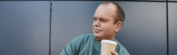 Ein inklusiver Mann mit nachdenklichem Gesichtsausdruck hält eine Kaffeetasse und genießt einen Moment der Ruhe in seinem geschäftigen Tag. — Stockfoto