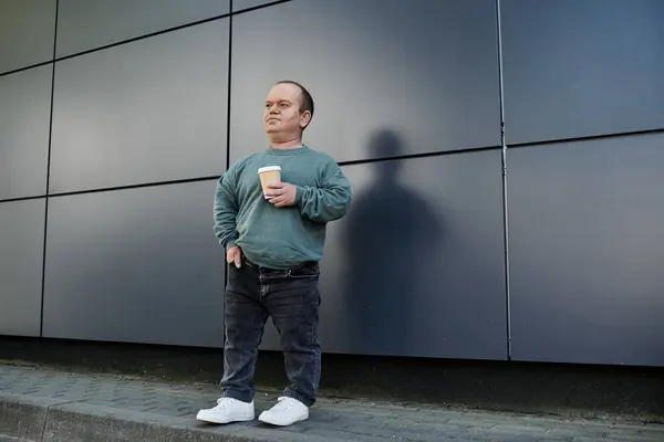 A man with inclusivity stands outside on a city street, holding a cup of coffee. — Stock Photo