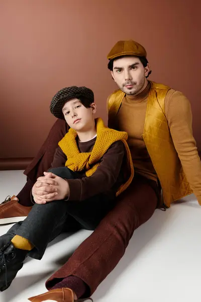 A father and son sit together on a white surface, both wearing brown and gold clothing. — Stock Photo