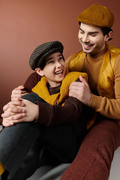A father and son share a joyful moment, laughing together while wearing matching caps. — Stock Photo