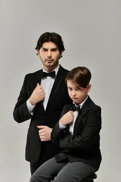 A father and son pose in matching tuxedos, the son sitting, the father standing. — Stock Photo