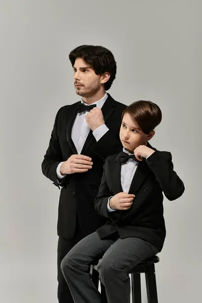 A father and his son stand side by side, both dressed in black suits and bow ties, ready for a formal event. — Stock Photo