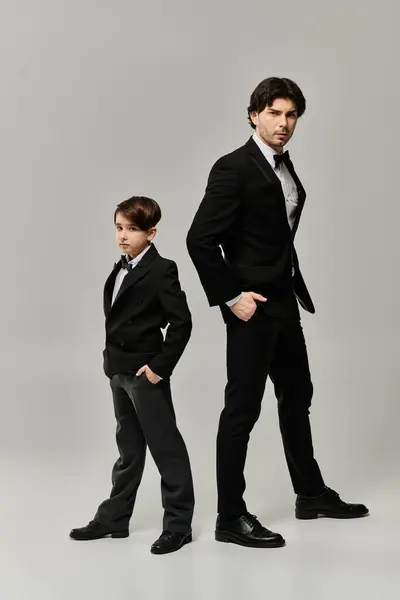 A father and son stand side-by-side in matching black suits, showcasing a strong bond. — Stock Photo