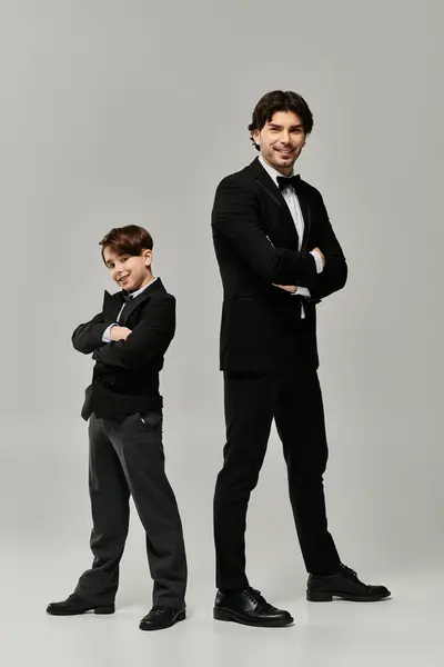 A father and son in formal attire, standing side-by-side against a gray backdrop. — Stock Photo