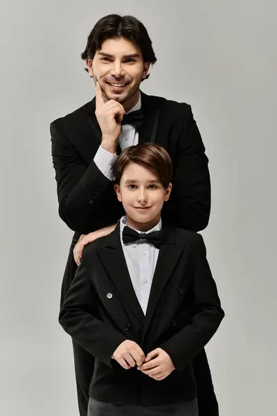A father smiles proudly as he stands beside his son, both dressed in tuxedos. — Stock Photo