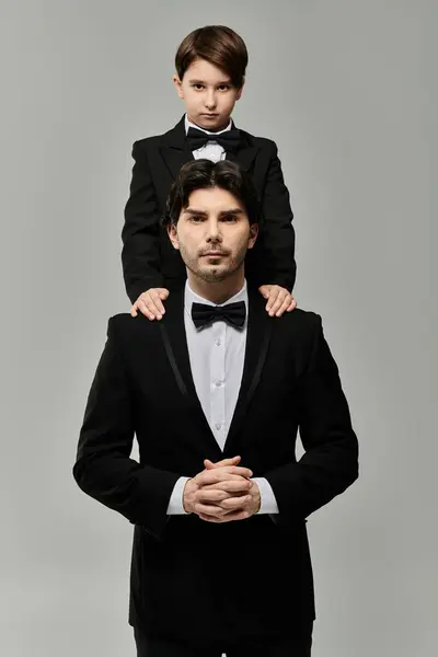 Un padre y un hijo en trajes a juego, con el hijo sentado sobre sus hombros padres. - foto de stock