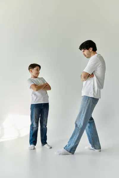 Vater und Sohn stehen zusammen in einem weißen Raum, beide tragen weiße T-Shirts und Jeans. — Stockfoto